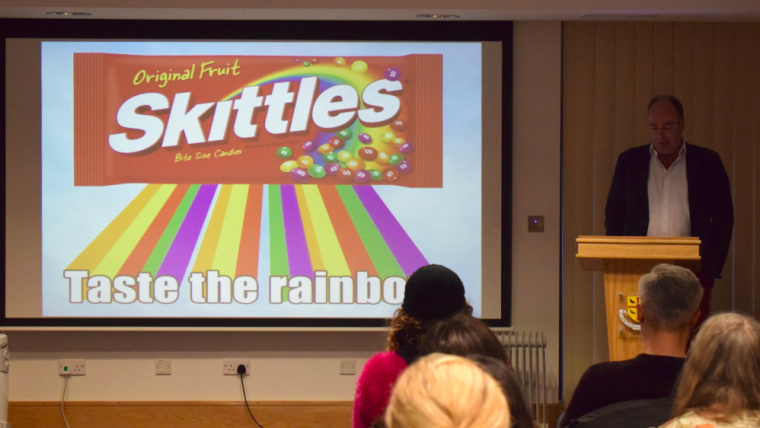 Man presenting with Skittles sweet packet on screen